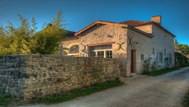 A stone house with a red door, a small window, and a gravel driveway. - Renovated stone house with swimming pool - 150 m from the medieval castle of Larressingle (Larressingle)