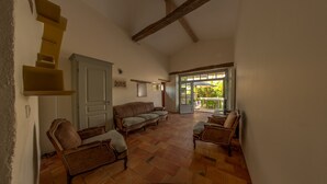 A spacious room with a high ceiling, a wooden staircase, a sofa, two armchairs, and a door leading to an outdoor patio area. - Renovated stone house with swimming pool - 150 m from the medieval castle of Larressingle (Larressingle)