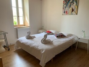 Une chambre avec un grand lit, deux oreillers en forme de cygne, un tableau abstrait aux couleurs vives accroché au mur, et une fenêtre avec des stores.