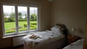 Een slaapkamer met een groot raam, een bed, een nachtkastje en een lamp.