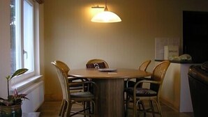Een eethoek met een ronde tafel, zes stoelen, een hanglamp en een raam met zonwering.