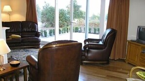Een woonkamer met een donkerbruine leren bank, twee leren fauteuils, een houten salontafel en een televisie op een houten kast.