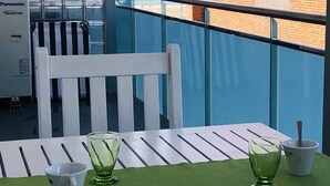 Un balcon avec une chaise blanche, une table avec des sets de table verts et deux verres verts.