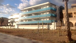 Un immeuble à plusieurs étages doté de balcons, d’un palmier et d’une zone pavée devant l’entrée.