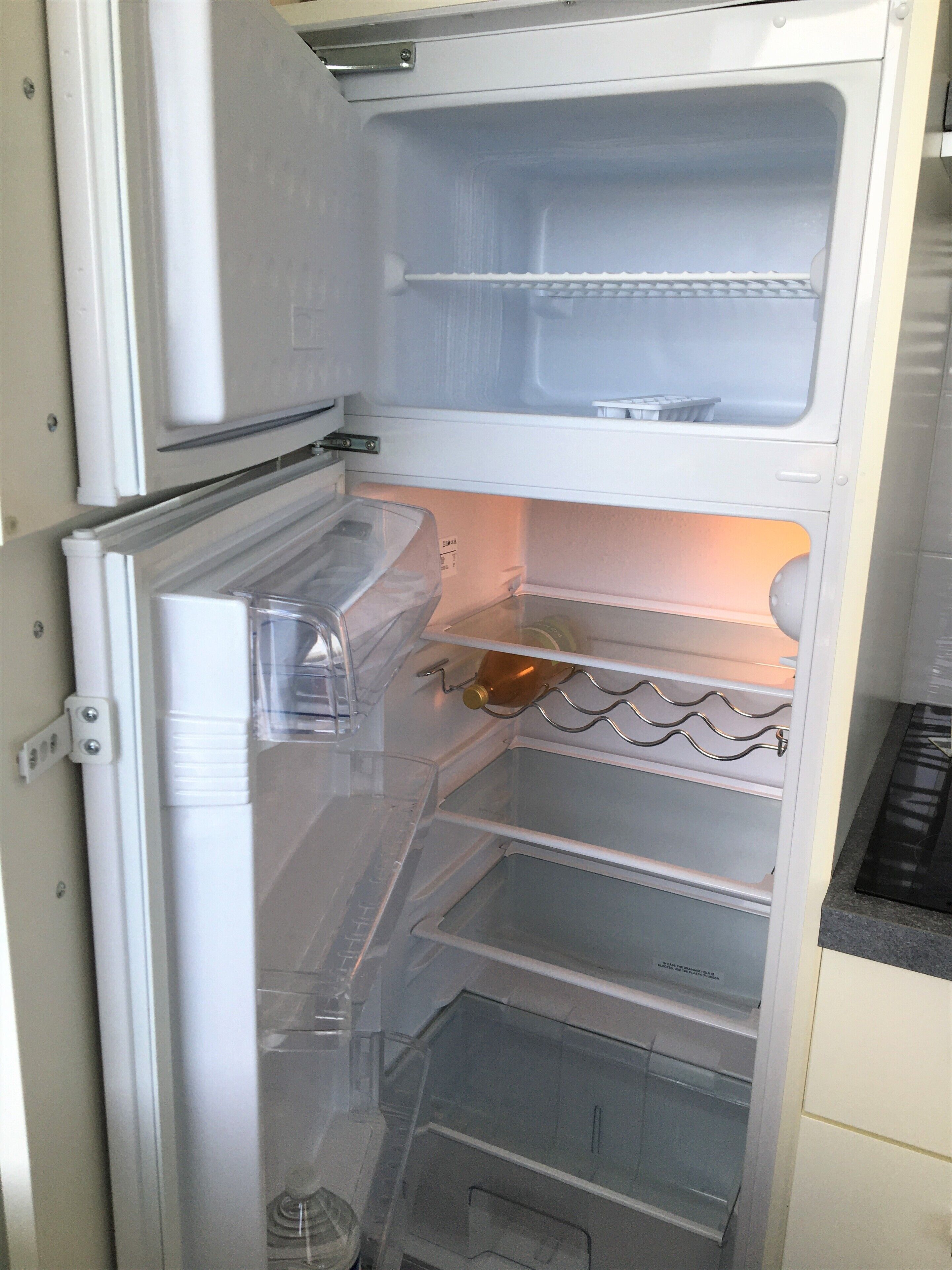 Een open koelkast met heldere planken en een waterdispenser.