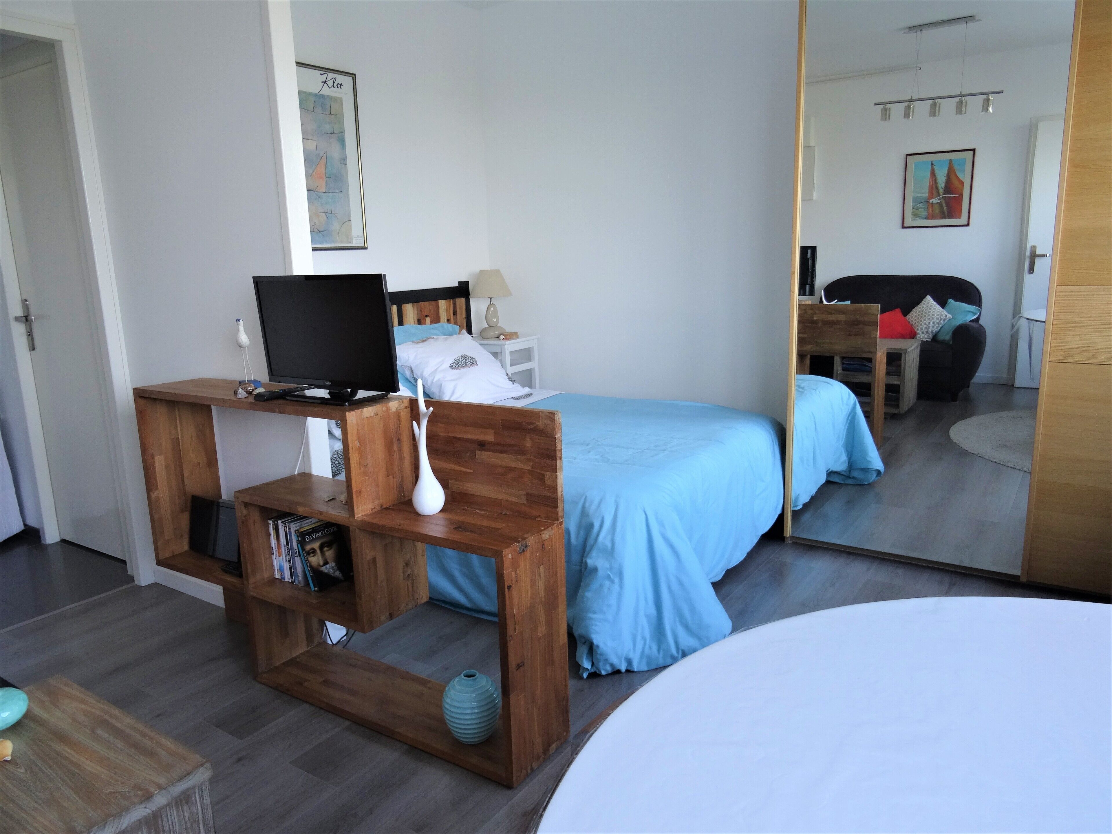 A bedroom with a bed, a desk with a computer, a mirror, and a TV.