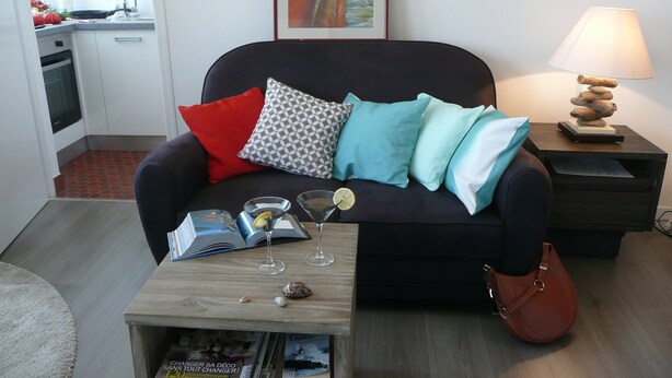 A living room with a sofa, a coffee table with magazines, a lamp, and a painting on the wall. - Studio 3*, SEA VIEW and facing the dragon, 150m from the BEACH, near the 2 caps site (Calais)