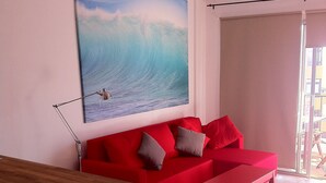 Una sala de estar moderna con un sofá rojo, una mesa de centro de madera y un cuadro de una ola en la pared.