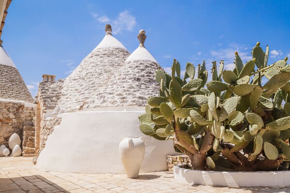 Un bâtiment traditionnel en pierre, doté de toits coniques, d’un cactus et d’un vase blanc.