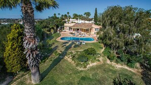 Un'ampia casa circondata da un prato curato e alberi, con una piscina.