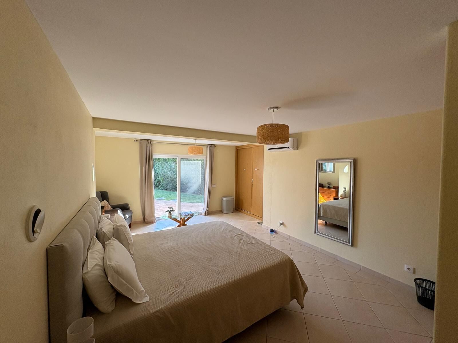 A bedroom with a large bed, a sliding glass door to a balcony, a ceiling fan, and a wall-mounted mirror.