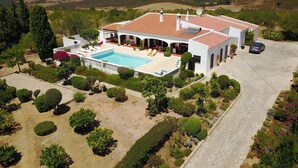 Una casa grande con piscina, rodeada de jardines cuidados y vistas a colinas onduladas.