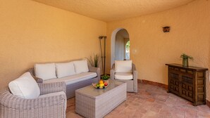 A sunlit patio with wicker furniture, a small table with fruit, and a cabinet.