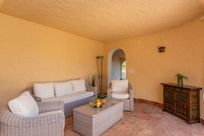 A sunlit patio with wicker furniture, a small table with fruit, and a cabinet.