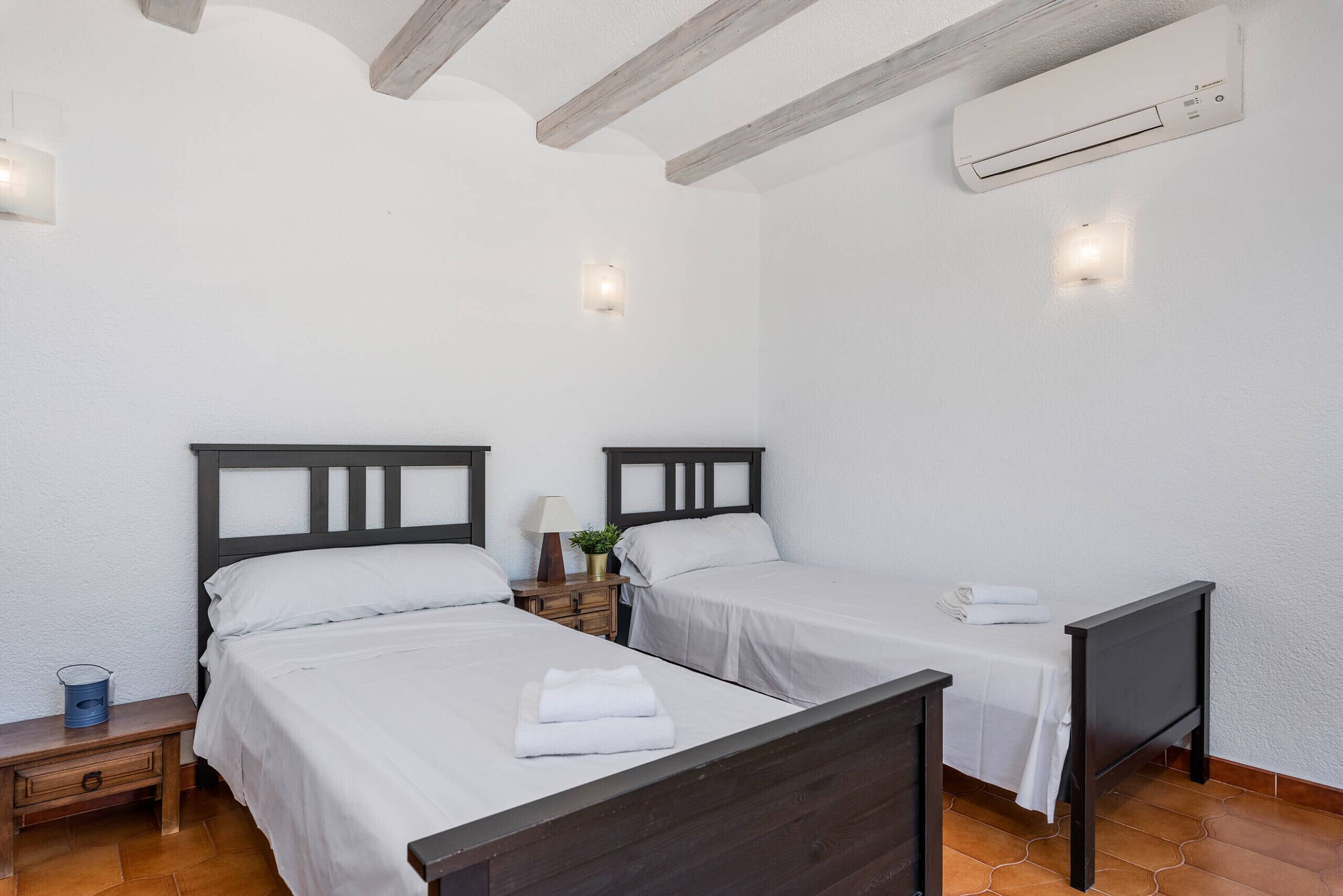 A room with two beds, a nightstand with a lamp, and an air conditioning unit.