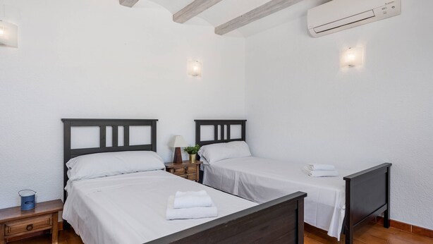 A room with two beds, a nightstand with a lamp, and an air conditioning unit.