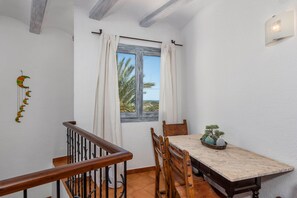 Uma sala de jantar com mesa, cadeiras e vista para palmeiras pela janela.