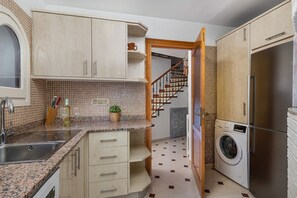 A compact kitchen with a built-in washing machine, a sink, and a countertop with a plant.