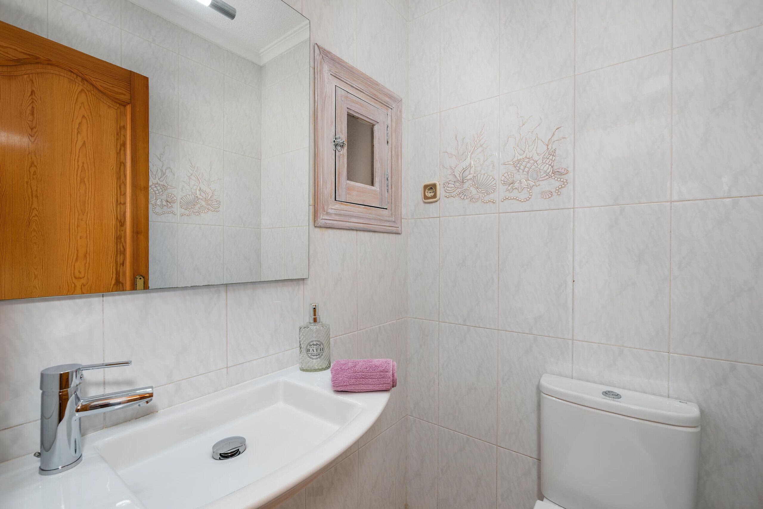A bathroom with a white sink, a mirror, a toilet, and a wooden cabinet.