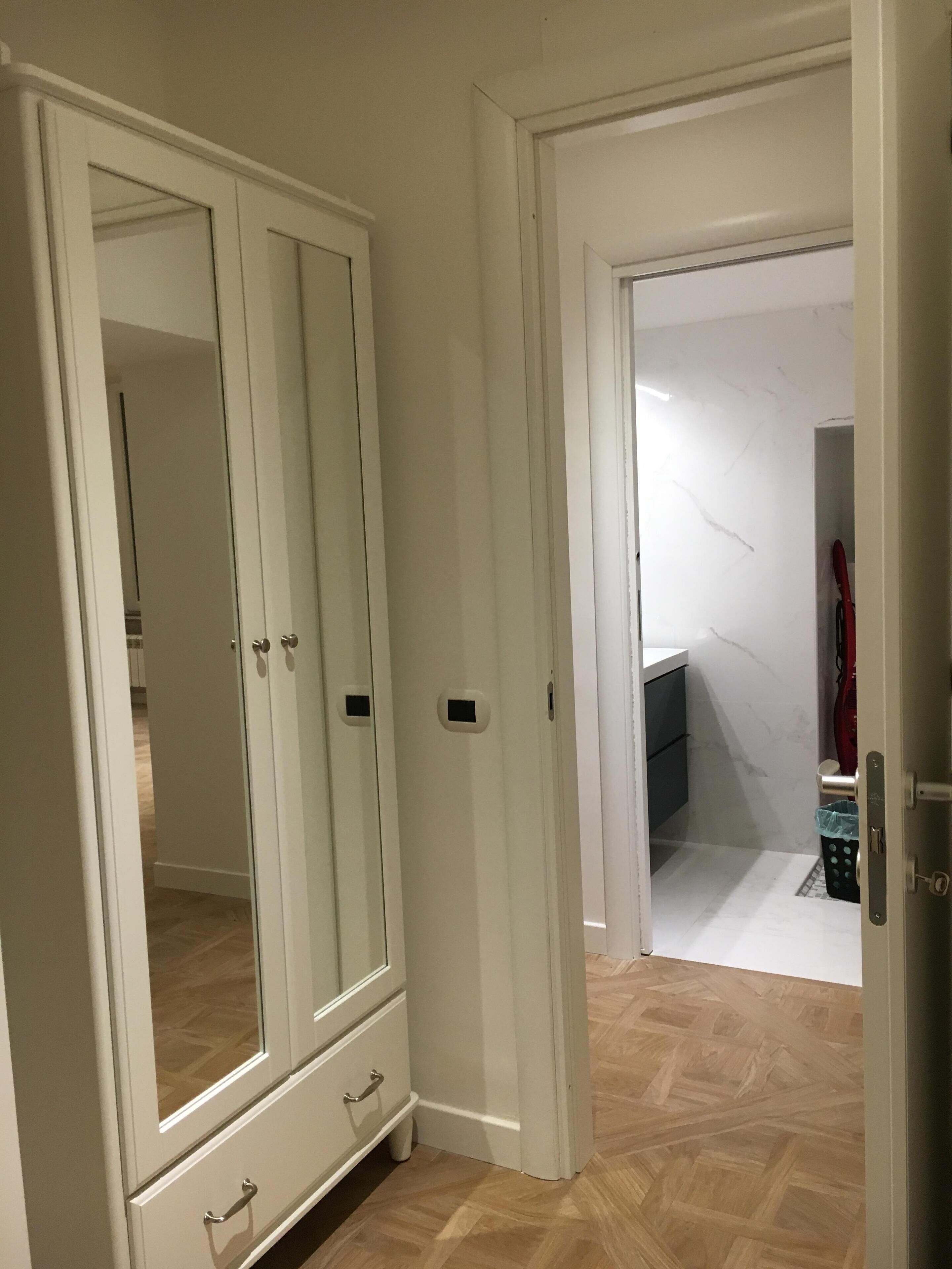 A room with a large wardrobe, a door leading to another room, and a tiled floor.