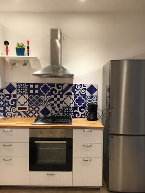 A kitchen with a gas stove, oven, stainless steel refrigerator, and decorative blue and white tiles. - Fafà Apartment in Spaccanapoli (Napoli)
