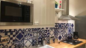 A kitchen with a microwave, stove, sink, and decorative tiles. - Fafà Apartment in Spaccanapoli (Napoli)