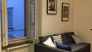 A living room with a grey sofa, a radiator, and a window with shutters. - Fafà Apartment in Spaccanapoli (Napoli)