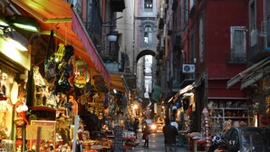 A narrow street lined with shops and balconies, leading to a building with a dome. - Fafà Apartment in Spaccanapoli (Napoli)
