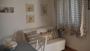Un salón acogedor con un sofá, una mesa de comedor con un cuenco y tres láminas botánicas enmarcadas en la pared.