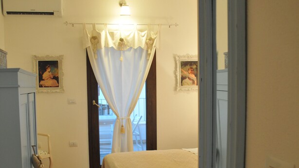Un dormitorio con cama, armario, silla y ventana con cortinas.