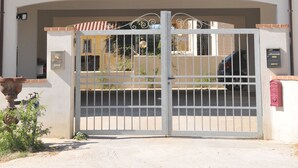 Un edificio de dos pisos con balcones, una entrada protegida por un portón y un cielo despejado.