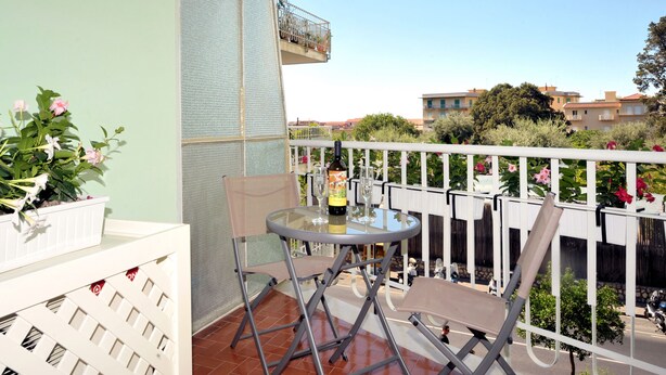 A balcony with a glass table, chairs, and a bottle of wine.