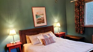 Un lit bien fait, avec une tête de lit en bois, deux tables de chevet avec des lampes, un tableau encadré au mur et une fenêtre avec des rideaux.