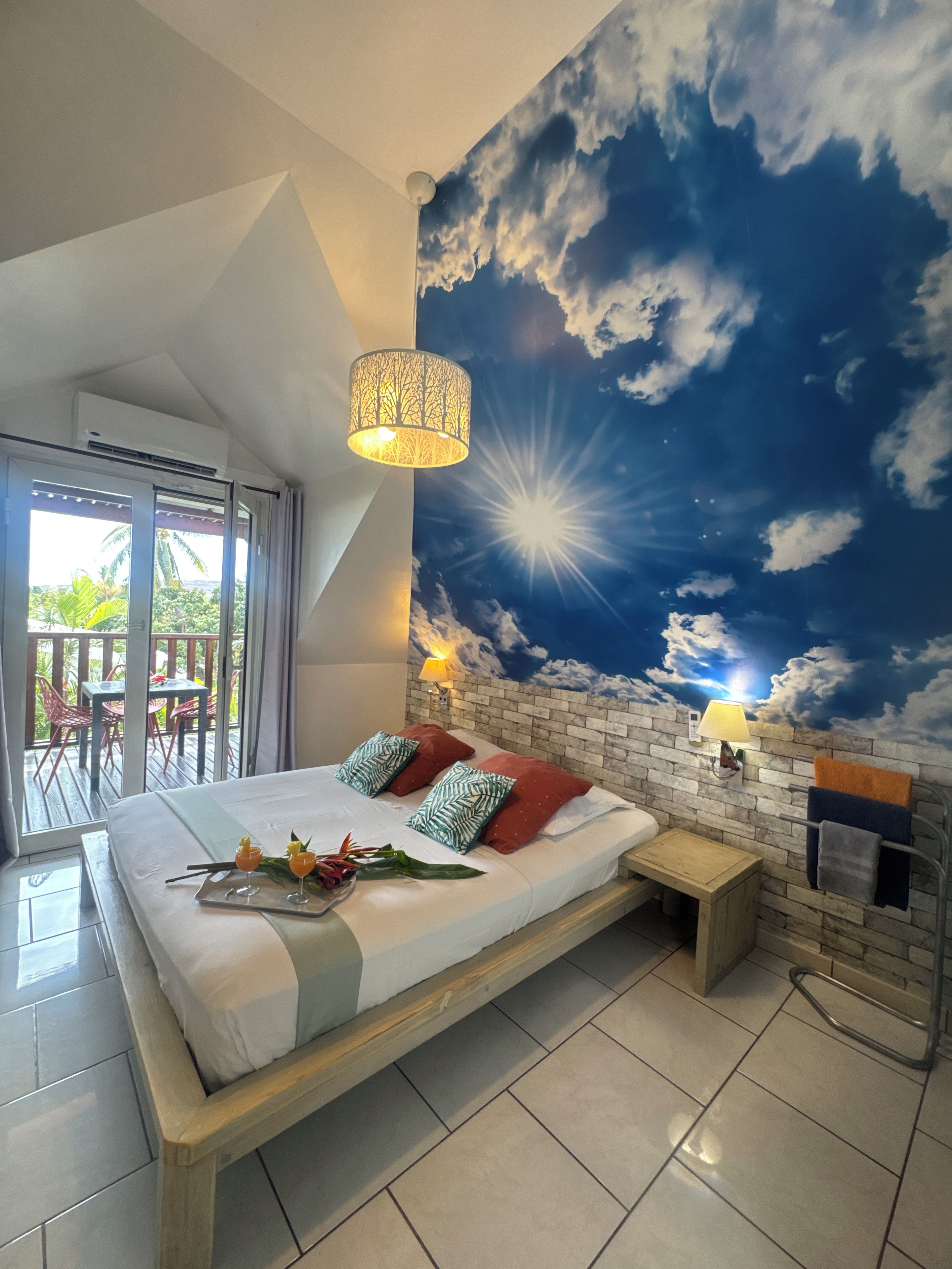 Een slaapkamer met een bed, een nachtkastje, een wandlamp en een plafonddecoratie van een lucht met wolken.