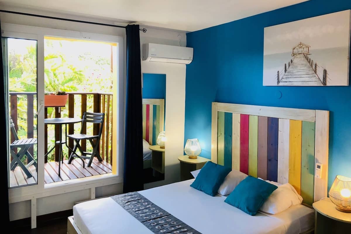 A bedroom with a large bed, a view of a balcony with outdoor furniture, and a colorful striped headboard.