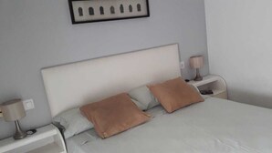 Una cama bien hecha con dos almohadas, una mesita de noche con una lámpara y un cuadro enmarcado en la pared.
