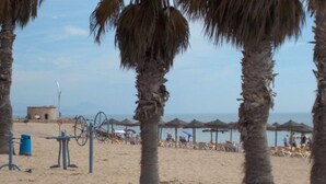 Una playa con palmeras, sillas de playa, sombrillas y un pequeño edificio al fondo.