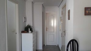 Un pasillo estrecho con una puerta blanca al final, una planta pequeña sobre un mueble y dos cuadros en la pared.