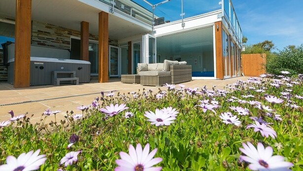Een modern huis met een patio, zitgedeelte buiten en een tuin vol bloemen.