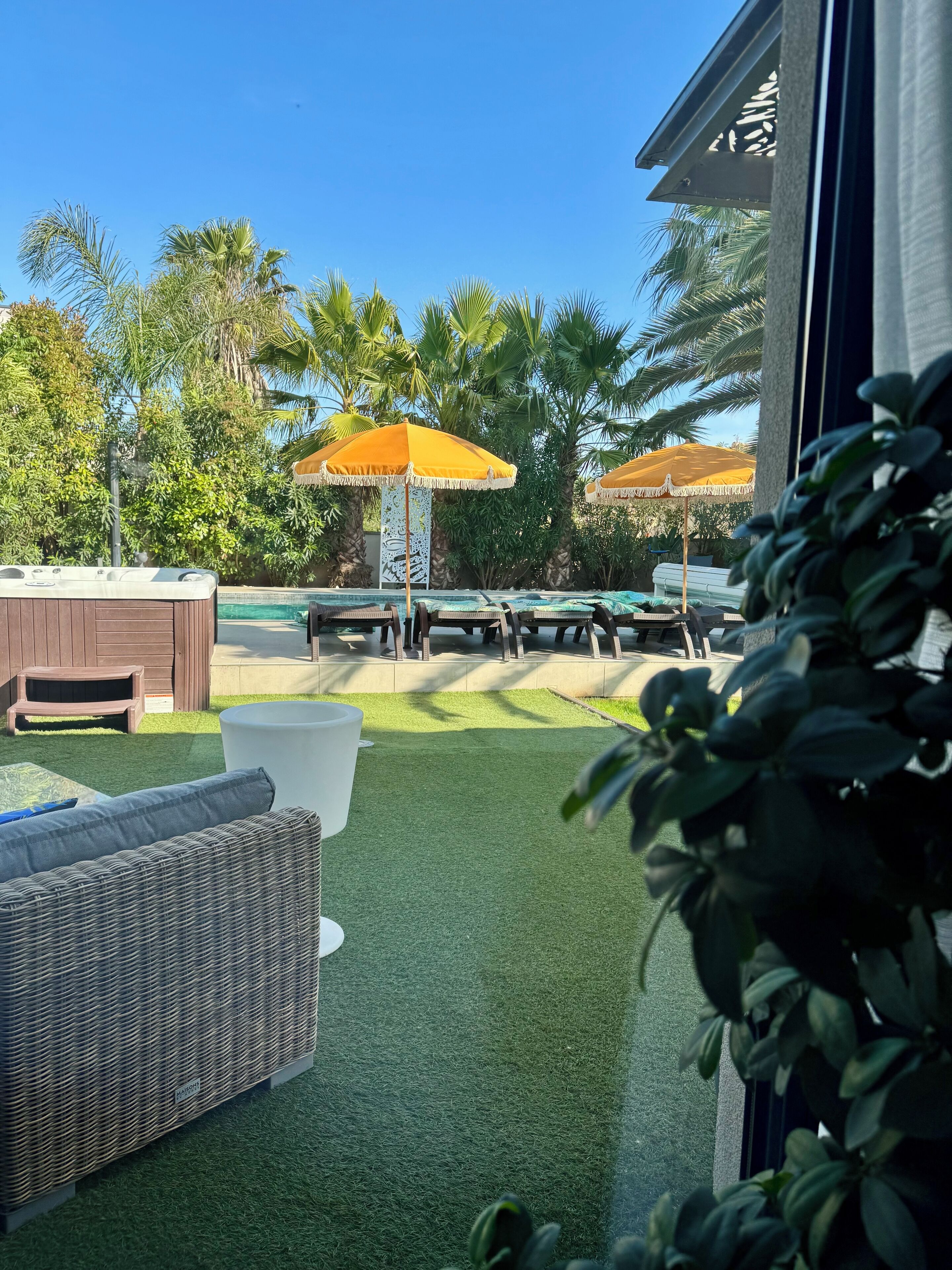 Un espace extérieur aménagé en terrasse, avec du gazon synthétique, un jacuzzi et deux parasols jaunes.