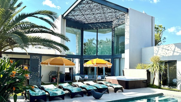 A modern pool area with lounge chairs, a hot tub, and a pergola.