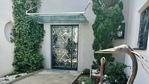 A courtyard with a decorative glass door, a concrete pathway, and a variety of plants including a prominent bird sculpture.