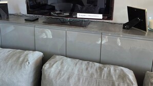 Una sala moderna con un televisor de pantalla plana grande montado en un mueble gris, un sofá y una pequeña mesa con un control remoto.