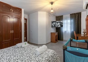 Hotellihuone, jossa on sänky, vaatekaappi, televisio ja pieni pöytä tuolilla.