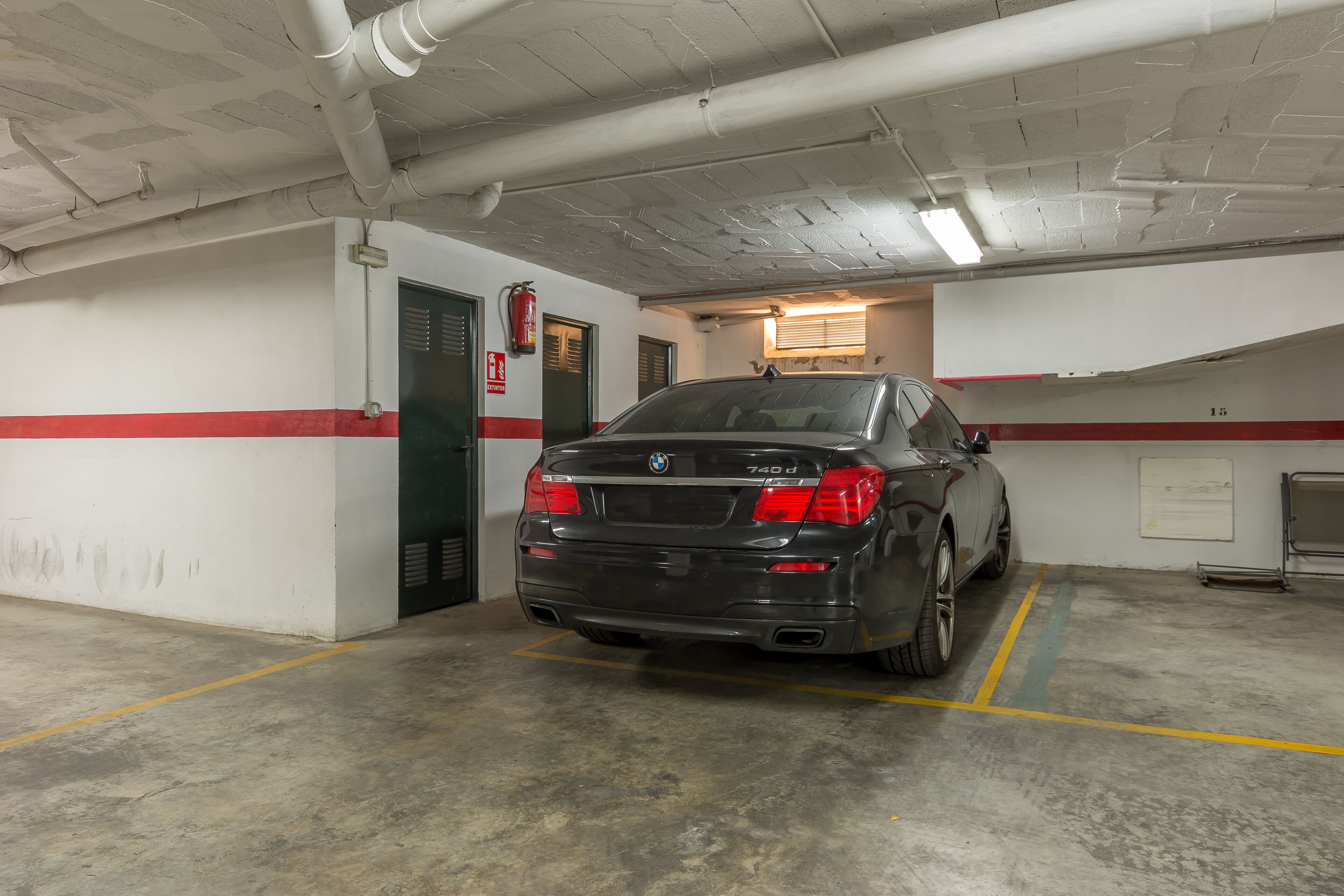 Une BMW 740d est garée dans un parking souterrain dont le sol est en béton et les murs sont blancs.