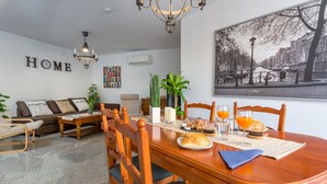 A dining area with a wooden table, chairs, and a breakfast setting including a croissant, orange juice, and a plate of food. - SF CARIHUELA LUXURY SUITE (Torremolinos)
