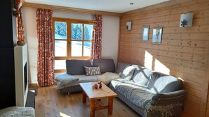 A cozy living room with a grey sofa, a wooden coffee table, and a window with patterned curtains. - LES ARCS1950 Very confortable apartment, Southview, snow sure, Indoorpool, Sauna (Bourg-Saint-Maurice)