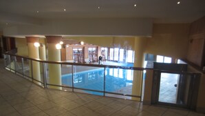 A spacious indoor area with a swimming pool, a balcony with a railing, and a view of a building with multiple windows. - LES ARCS1950 Very confortable apartment, Southview, snow sure, Indoorpool, Sauna (Bourg-Saint-Maurice)
