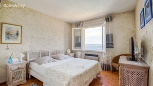 Een slaapkamer met een bed, nachtkastjes, een televisie en een raam met gordijnen.