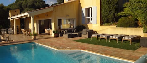 A poolside area with a pool, outdoor furniture, and a building with windows and shutters.